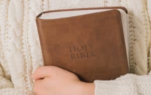 woman holding brown bible in arms